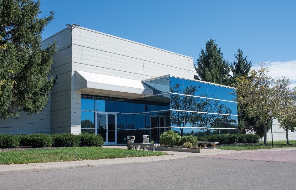 The exterior of a commercial office building with dark tinted windows that reflect the trees. 